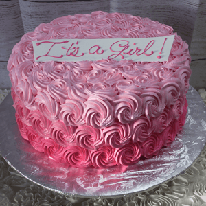 The BD-062 Pink rosette is a round cake with pink buttercream rosettes and an "It's a Girl!" sign on top, presented on a silver cake board.