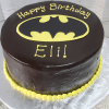 The CB-006E is a round chocolate cake featuring a yellow Batman logo, “Happy Birthday Eli!” in yellow icing on top, and a border of yellow icing dots around the base.