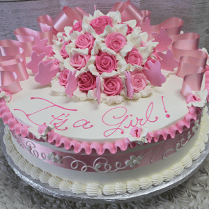 BB-002 is a round cake with pink and white frosting, decorated with pink and white roses, pink bows, a floral border, and "It's a Girl!" written in pink icing.
