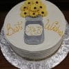The BR-057 is a round cake with a mason jar design, yellow flower decorations, "Best Wishes" in yellow icing, and "K & B" on the jar. Presented on a silver textured board.