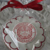 The GC-080G Northeastern University is a round cookie featuring the university's red and white seal, wrapped in clear plastic with a red ribbon, displayed on a white textured surface.