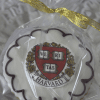 The GC-080K Harvard is a round cookie with scalloped white icing and maroon accents, featuring the Harvard University crest. It's wrapped in clear plastic and tied with a gold ribbon.