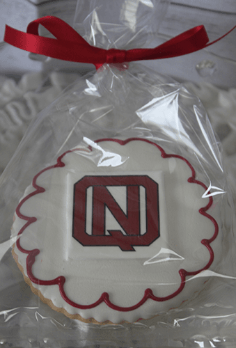 The GC-080D North Quincy High School is a round sugar cookie with white icing, a red border, and a red/black "N" in the center, wrapped in clear plastic with a red ribbon.