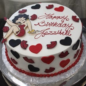 Round birthday cake (BD-140) decorated with red hearts, black and red lips, and a cartoon woman in a red dress. "Happy Birthday Jezzibell" is written in red icing on top.