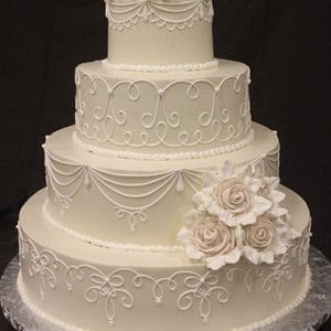 The WC-033 is a three-tiered white wedding cake with intricate piped icing, topped with white sugar roses and more sugar roses decorating the bottom tier.