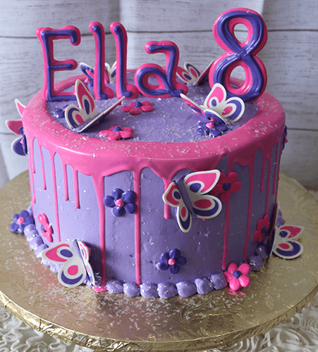 CB-024C: A purple birthday cake with pink icing drips, decorated with butterflies, flowers, “Ella,” and a large number 8 topper on a gold cake board.