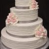 WC-040 is a four-tiered white wedding cake featuring textured icing, adorned with light pink and white rose flowers, and finished with silver ribbon wrapping each tier.