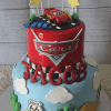 The TC-022 is a two-tier Cars-themed birthday cake with a Lightning McQueen topper, stars, Route 66 signs, cacti, clouds, and "Jacob" in bold red letters.