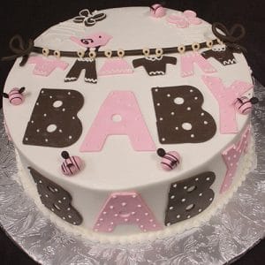 BB-020: Round cake featuring "BABY" in bold pink and brown letters, polka dots, fondant baby clothes on a clothesline, and small pink-brown fondant balls on a silver patterned board.