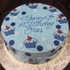 The CB-025D is a round blue cake with polka dots, cupcake designs, and "Happy Birthday OM" in blue icing, presented on a silver-patterned board.