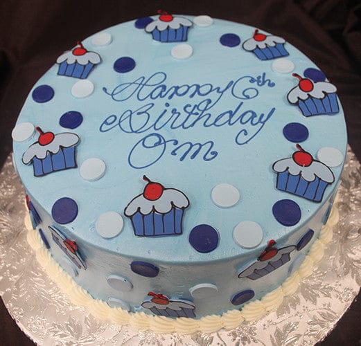 The CB-025D is a round blue cake with polka dots, cupcake designs, and "Happy Birthday OM" in blue icing, presented on a silver-patterned board.