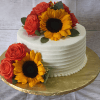 The BR-063 is a white frosted cake adorned with yellow sunflowers and red roses, set on a gold textured cake board against a light wooden background.