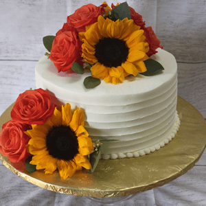 The BR-063 is a white frosted cake adorned with yellow sunflowers and red roses, set on a gold textured cake board against a light wooden background.