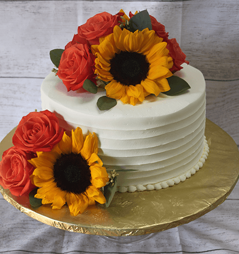 The THX-033 is a white frosted cake adorned with bright yellow sunflowers and vibrant red roses, presented on a gold cake board against a light wooden background.