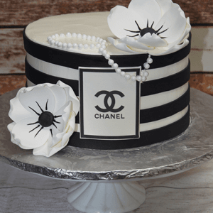 The BD-033B Designer Black/White cake features black and white stripes, two white fondant flowers, edible pearl accents, and a Chanel logo plaque, presented on a white cake stand.