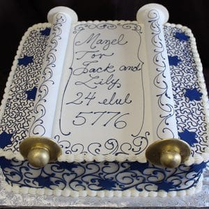 RC-090: Rectangular cake styled as a Torah scroll with blue and white designs, gold handles, and inscription “Mazel Tov Jack and Lily 24 Elul 5776.”.