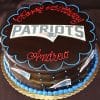 The ST-001 Patriots Ganache is a chocolate cake with blue icing, decorated with the New England Patriots logo and blue dots. "Happy Birthday Andrew" is written in red icing on top, with more Patriots logos on the sides.