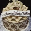 The BD-048 cake features brown and gold flowers, a large “25” topper, ruffled icing border, and a white “Happy Birthday Kathleen” banner in cursive, presented on a silver-patterned board.