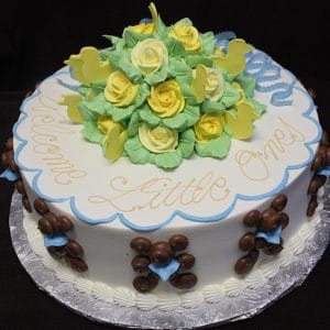 The BB-003 cake is round with yellow and white icing roses, green leaves, and yellow bird shapes on top. "Welcome Little Ones" is written in yellow icing, with chocolate and blue decorations along the sides.