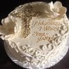 RC-024: Round white cake featuring ornate scrollwork, two large white flowers, a gold cross, and "God Bless Patrick Sean Joseph" written in gold icing. Presented on a silver patterned board.