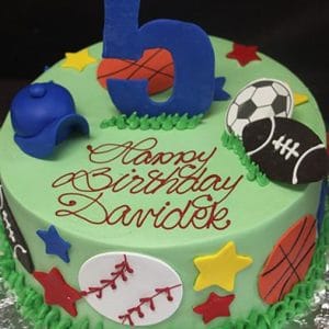 The ST-009 Assorted Sports cake features a green base, sports balls decorations, colorful stars, a blue cap, a large blue number 5 topper, and "Happy Birthday Davidek" written in red icing.