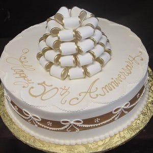 BD-164 is a round white cake featuring gold-trimmed white ribbon loops on top, gold "Happy 50th Anniversary" writing, and a brown ribbon with white bow designs around the sides.