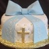 The RC-059 is a round white cake with a large blue fondant bow, gold accents, a gold cross on the side, and "God Bless Sendel" written in white script on the blue ribbons.