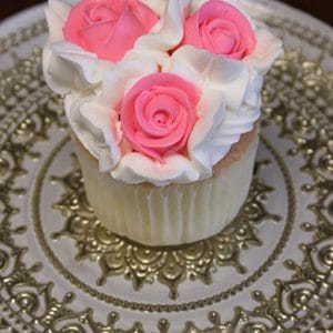 A CC-016 chocolate cupcake with white chocolate mousse filling, topped with three pink rose-shaped icing flowers, is displayed on an ornate gold and white patterned plate.