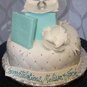 The BR-016 is a white quilted cake with silver dots, topped with a large white flower, light blue gift boxes, and a ring; a banner at the base reads "Congratulations, Melissa & Jack.