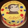 The CB-009N is a round yellow birthday cake with red and blue polka dots, featuring Curious George on top and "Happy 5th Birthday Aiden!" written in red icing.