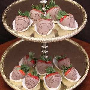 A two-tiered gold dessert stand displays ST-001 Milk Chocolate Strawberries, each in a white paper cup with chocolate drizzle, arranged neatly on both tiers.
