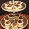 A two-tiered gold serving tray displays Pecan Tarts, each topped with chocolate drizzle and cream, arranged neatly on both levels against a dark background.