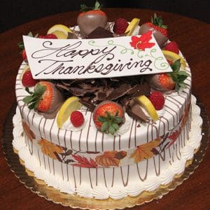 The THX-004 Display Lemon Raspberry cake with Fall Decor features a round Thanksgiving design topped with chocolate-dipped strawberries, lemon wedges, chocolate shavings, autumn leaves, and a "Happy Thanksgiving" card.