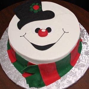 CH-020 is a round cake designed as a snowman's face with a black hat, big smiling mouth, red nose, and green and red scarf, presented on a silver patterned board.