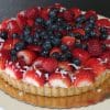 The GD-022 Mixed Berry Fruit Tart features fresh strawberries, blueberries, raspberries, and shredded coconut on top, presented on a gold board against a neutral background.