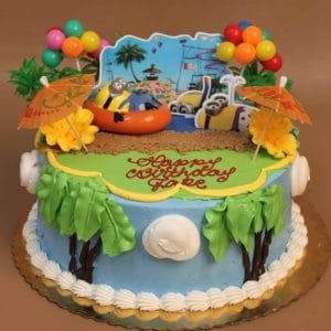 The SC-039 Minions birthday cake features tropical decorations with palm trees, umbrellas, balloons, and Minion figures for a beach theme. "Happy Southcoast Jobe" is written in red icing on the green top.