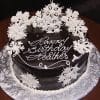 A round chocolate cake (CH-015) with white icing flower decorations and "Happy Birthday Heather" in elegant script on top, presented on a silver-patterned cake board.