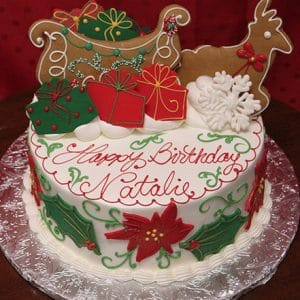 The CH-043 is a festive birthday cake with holly, poinsettias, green swirls, gift boxes, a sleigh, reindeer, and snowflake cookies. "Happy Birthday Natalie" is written in red icing.