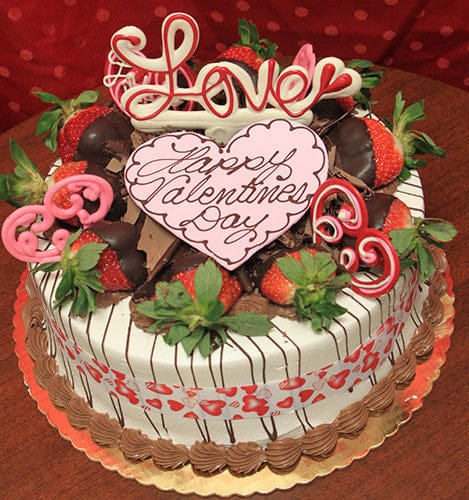 The VC-006 Display Strawberry Grand Marnier cake is a round Valentine’s Day cake topped with chocolate-dipped strawberries, pink and red heart decorations, and a large heart-shaped plaque that reads "Happy Valentines Day" with "Love" on top.
