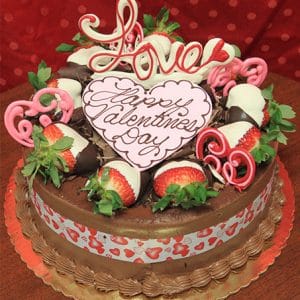 The VC-007 Display Tiramisu cake with Valentine's decor features chocolate-dipped strawberries, pink heart-shaped chocolates, a white chocolate "Happy Valentines Day" plaque, a Love topper, and a heart-patterned ribbon around the side.