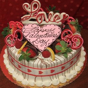 The VC-004 Display Gold cake features lemon raspberry mousse and is decorated with strawberries, chocolate, a pink heart reading "Happy Valentines Day," "Love" in pink icing, and a heart-patterned ribbon.