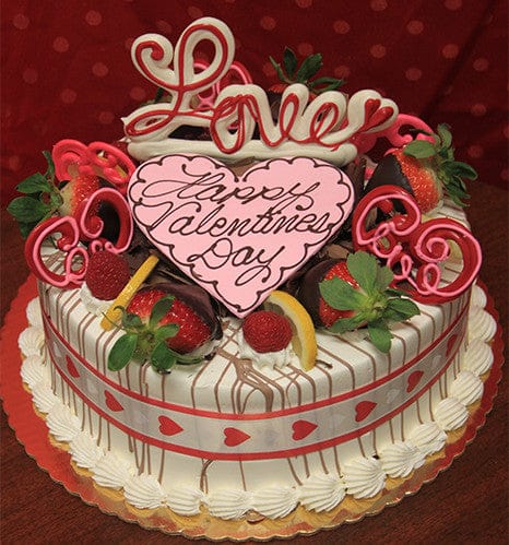 The VC-004 Display Gold cake features lemon raspberry mousse and is decorated with strawberries, chocolate, a pink heart reading "Happy Valentines Day," "Love" in pink icing, and a heart-patterned ribbon.