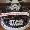 CB-007C: Round chocolate cake with white Star Wars lettering, lightsabers, Stormtrooper helmet, and "Happy Birthday Michael" banner; set on a silver board with white frosting dots.