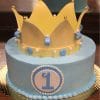 The CB-016C is a round blue cake topped with a yellow crown, white and blue accents, and a large blue number 1 on a white circle, perfect for first birthday celebrations.
