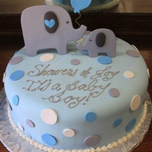 The BB-040 is a blue cake with polka dots, two elephant toppers, and a blue balloon. It features the message "Showers of Joy! It's a Baby Boy!" elegantly written on top.