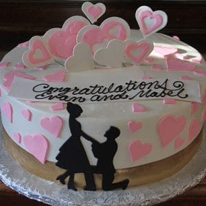 The BR-041 is a round cake with pink and white heart decorations, featuring a silhouette of a couple with one kneeling, and a “Congratulations Evan and Mabel” banner.