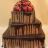 The TC-140 is a three-tier square chocolate cake with chocolate ganache drips, topped with fresh strawberries, blueberries, and raspberries, set against a beige background.