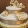 Celebrate a 50th anniversary with TC-151, a two-tiered white cake adorned with gold ribbons, pearls, three large gold and white flowers, and topped with a gold “50” decoration.
