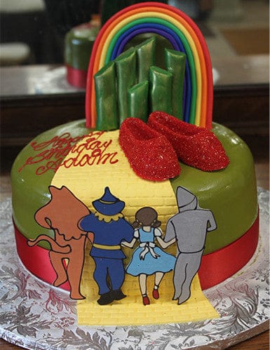 The CB-010C cake features Dorothy, the Tin Man, Scarecrow, and Cowardly Lion on a yellow brick road to emerald towers, topped with red ruby slippers and a rainbow for a Wizard of Oz theme.