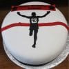 The ST-012 Running cake is round and white, featuring a silhouette of a runner with a "40" bib crossing a red finish line. A red banner on top says "Happy Birthday Durgesh" with black stars at each end.